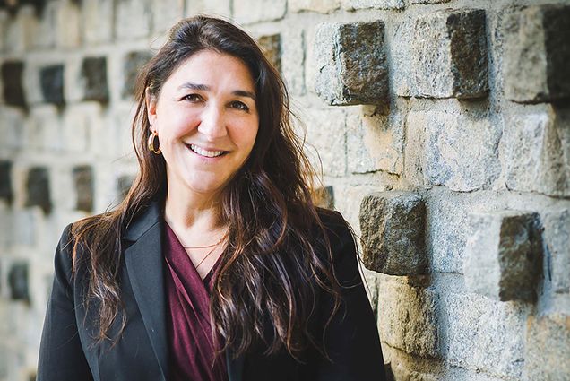 Photo of Carrie Landa, director of Behavioral Medicine and associate director of Student Health Services, is BU’s new executive director of student wellbeing. She wears a black blazer and crimson blouse and leans against a beige, brick wall.