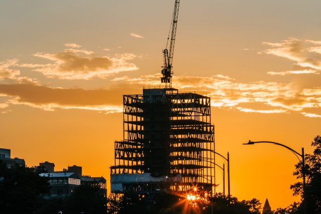 photo of BU’s new 19-story Center for Computing & Data Sciences during construction. A crane is atop the structure. It serves as a looming figure during a scenic orange sunset. Cars are seen in the horizon.