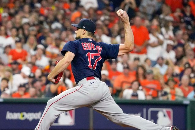 photo of Nathan Eovaldi of the Boston Red Sox pitching against the Houston Astros in Game 6 of the American League Championship Series at Minute Maid Park in Houston, Texas. The photo is snapped mid-pitch, as he wears a blue Red Sox uniform and blurry fans fill the background.