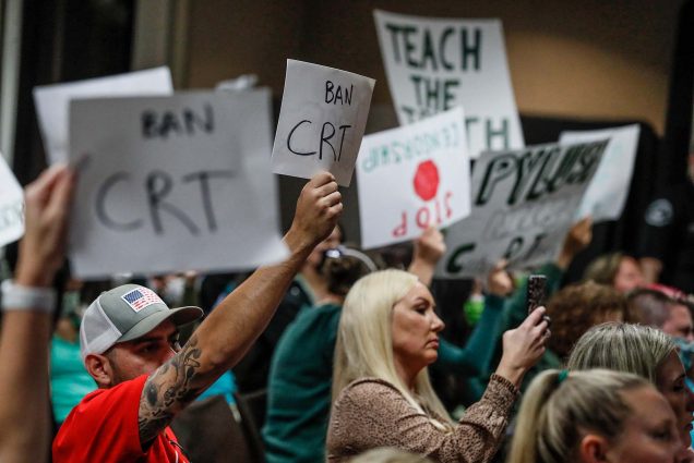 Photo of parents protesting during a meeting of the Placentia Yorba Linda School Board in which they discussed a proposed resolution to ban it from being taught in schools. Parents hold signs that say "BAN CRT"