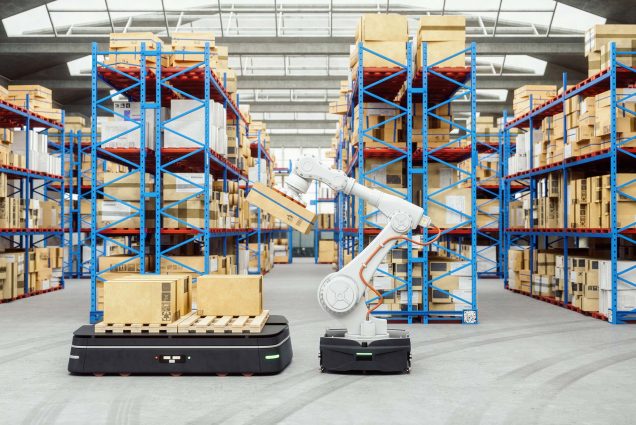 Photo of a white, automated robotic arm in the middle of a distribution warehouse, with blue racks piled high with cardboard boxes.