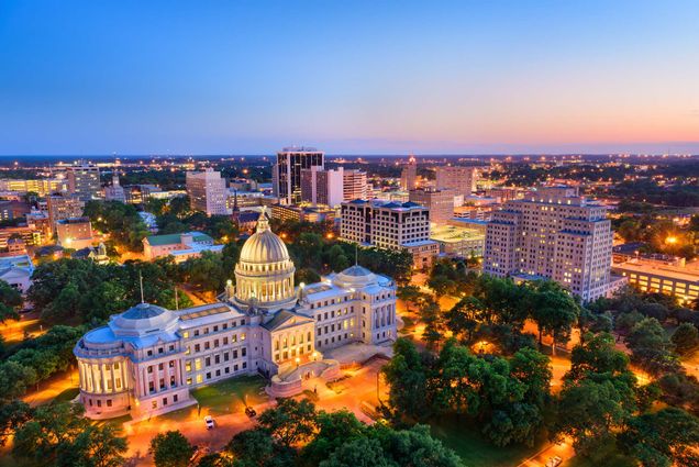 Aerial photo of Jackson, Mississippi, USA skyline over the Capitol Building. The capitol building is lit up with yellow lights.