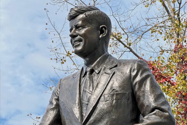 a bronze statue of John F Kennedy against a blue sky background