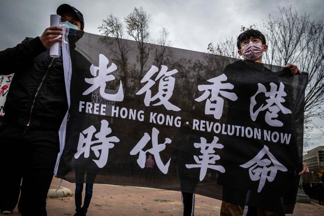 photo of 2 Hong Kongers holding a black flag frequently used during the city's 2019 pro-democracy protests, during a rally outside the White House in Washington, D.C. on Nov. 14, 2021. They both wear all black and have PPE masks on. The flag features Chinese characters and reads "Free Hong Kong - Revolution Now"