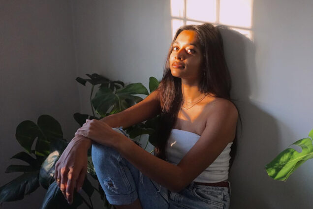 Sharmetha Ramanan sits in the sunlight in a white top and jeans