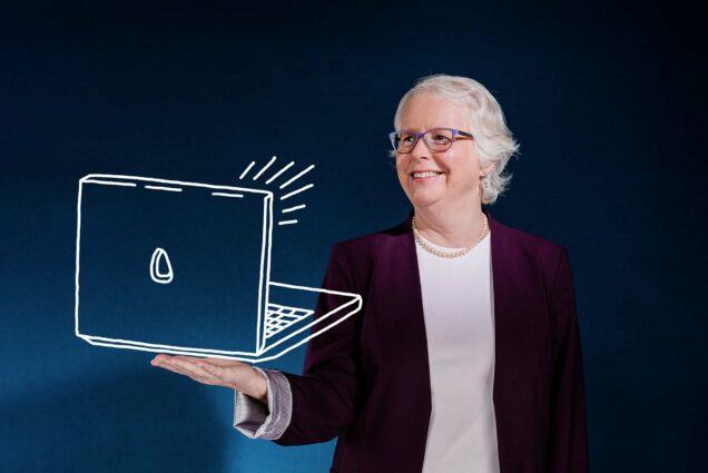 Photo of Jean Morrison, a white women in a white shirt and crimson blazer standing in front of a blue background with her hand extended. An illustration of a laptop is drawn over her extended hand. She smiles and has short white hair and glasses.
