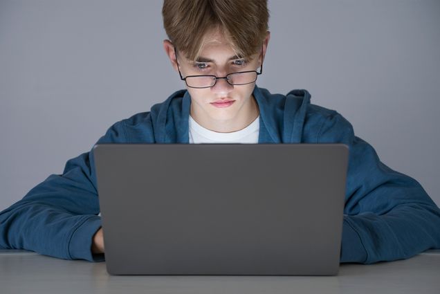 Teenage boy uses a laptop while doing his school work or homework, concept of online education