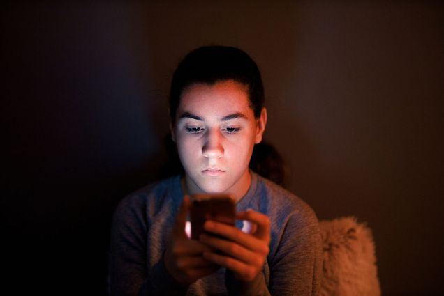 Photo of a young teenage girl using her smartphone in a dark room.