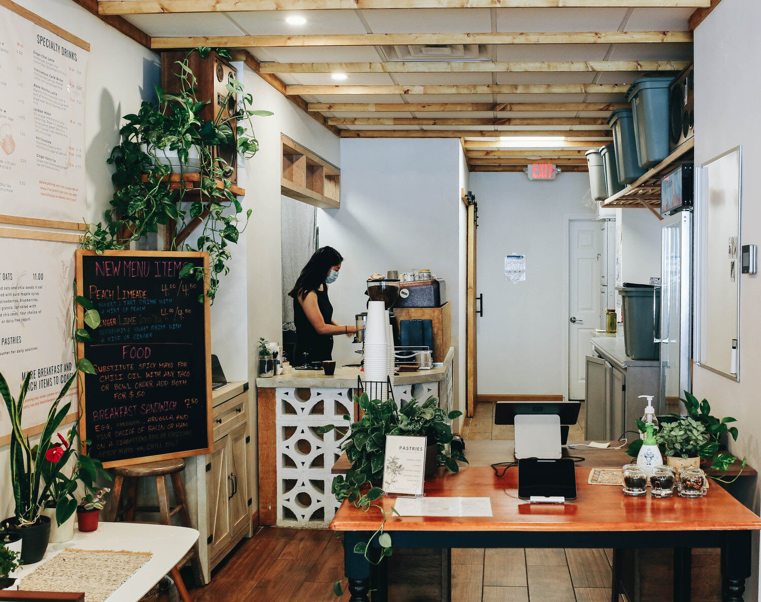 Photo: Interior of Glasser Coffee Co. A small bright coffee shop, with wood and greenery tones. A worker stands at the cash register as coffee paraphernalia  is on display.