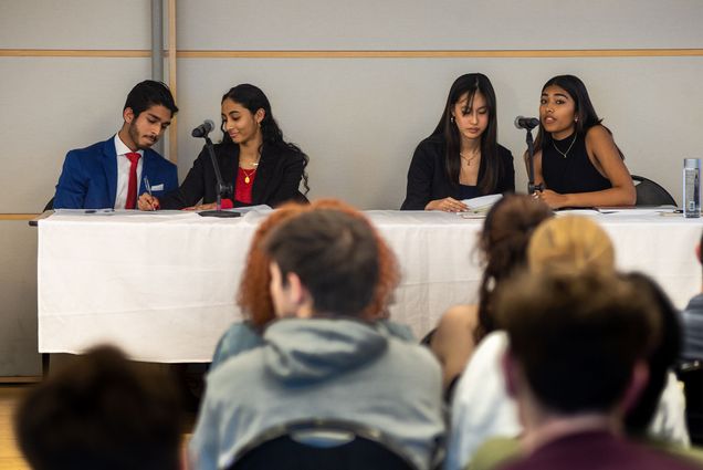 Students sit at a panel table at the BU Student Government Debate in front of a crowd