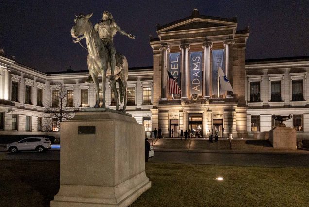 A picture of the museum of Fine Arts in Boston at dusk, with a statue of a person on a horse in front of a dramatic columned entrance