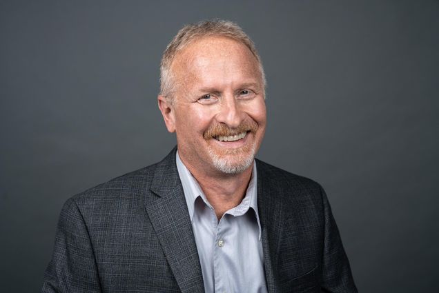 Headshot of Jerry Crasnick in a gray suit jacket suit, smiling, with a gray background.