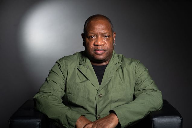 Louis Chude Sokei sits in front of a gray background in a green shirt