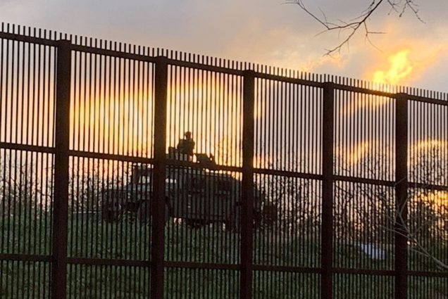 Photo of the playground on the campus of the University of Texas, Rio Grande Valley. A large barred fence shows a stationed army vehicle on the other side during a scenic sunset