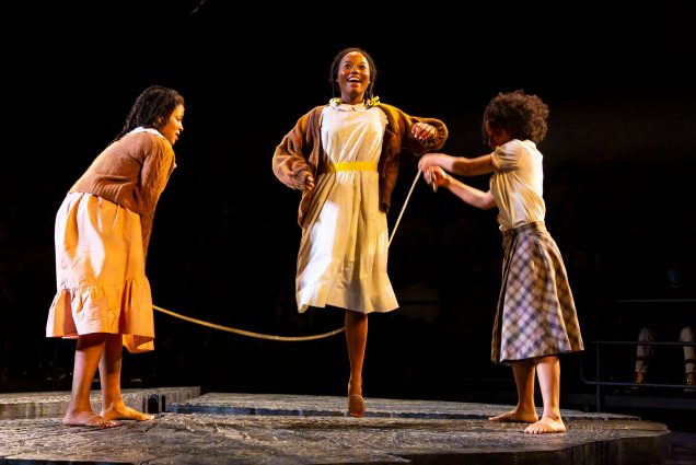 Photo of three young Black actress on stage, dressed in early 20th century garb, joyfully playing jump rope. Pictured are Brittany-Laurelle, Hadar Busia-Singleton, and Alexandria King who are all featured in The Huntington’s production of The Bluest Eye by Lydia R. Diamond, playing now through March 26 at the Calderwood Pavilion at the BCA, and available digitally through April 9 on huntingtontheatre.org.