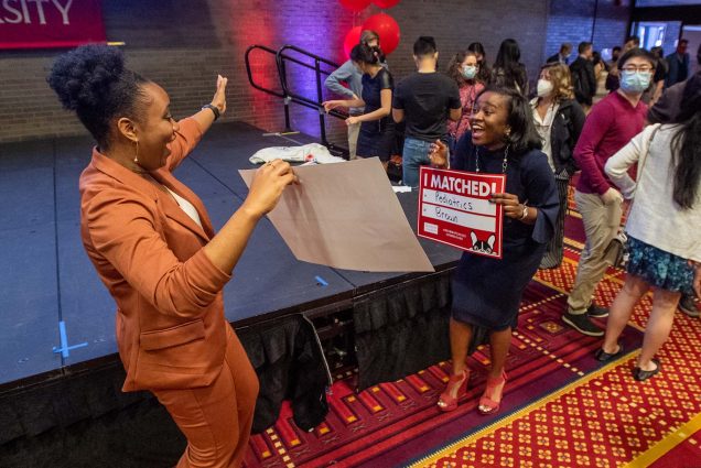 Photo of Nirisha Commodore, left, and Korede Yoloye reveal each others’ matches and celabrate on Match Day March 18 in the Metcalf Hall in the GSU. Commodore is a young Black woman wearing a burnt umber pant suite, with her hair pulled back in a bun; she extends her hands jubilantly and holds her match sign. Yoloye, a young Black woman with shoulder length hair wearing a black dress, is similarly exuberant and holds her "I Matched!" sign.