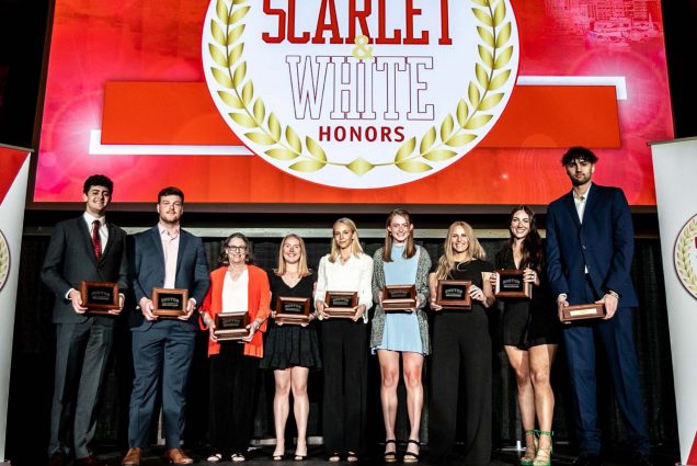 Photo of students dressed nicely, on stage, holding black, wooden plaques awards. Behind them on stage a large screen reads "Scarlet & White Honors"