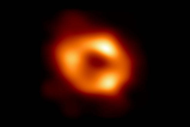 Image giving the first visual evidence of the presence of Sagittarius A*, the supermassive black hole at the center of our galaxy, captured by the Event Horizon Telescope (EHT) Collaboration. EHT Collaboration. In the image, a bright orange blob is seen, sort of resembling a donut, with three brighter yellow spots. The area around the orb is pitch black.
