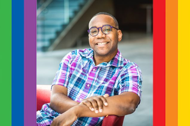 A picture of Vincent Stephens, wearing glasses and a blue plaid shirt. Rainbow stripes adorn the sides of the image