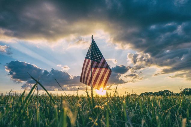 Photo of a small American flag stuck into a field of grass during sunset.