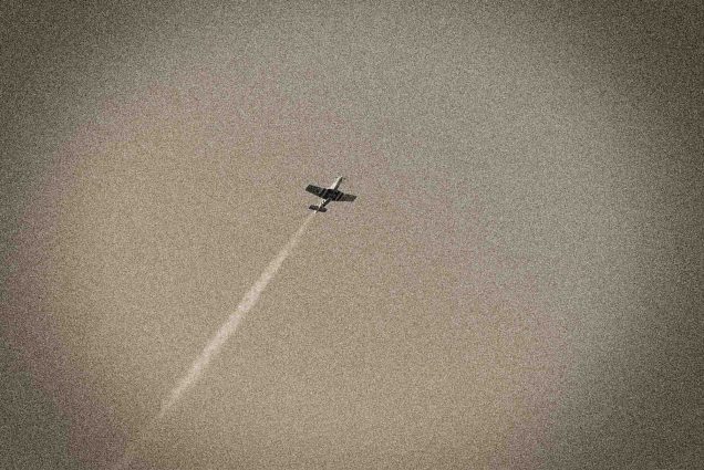 A WWII era plane flies through the sky with a vapor trail behind