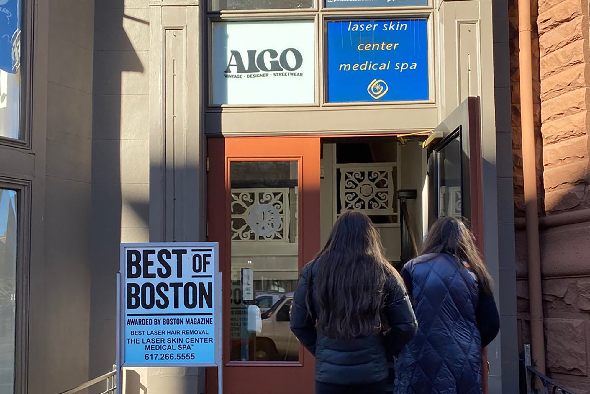 Photo: Two individuals in coats are entering a curbside store called Aigo.