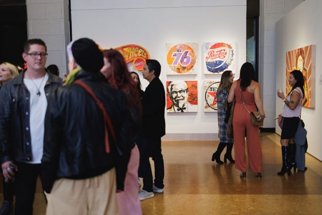 Photo of people congregating in an open art gallery. Some sit and stand as art is featured on the walls.