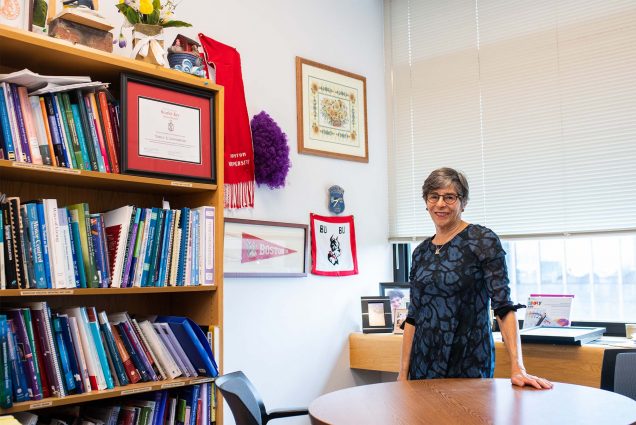 Nancy Lowenstein stands in her office on Boston University's campus, with various artifacts on a bookshelf nearby