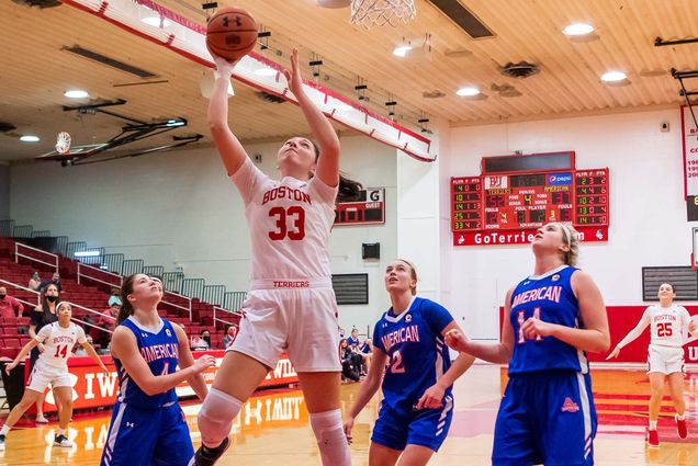 Photo: Women's basketball player Maren Durant jumps up to shoot a basketball into the hoop. She wears a white and red basketball jersey and shorts with the number 33 on the front of the jersey top. Three players in blue watch from around her as she takes her shot.