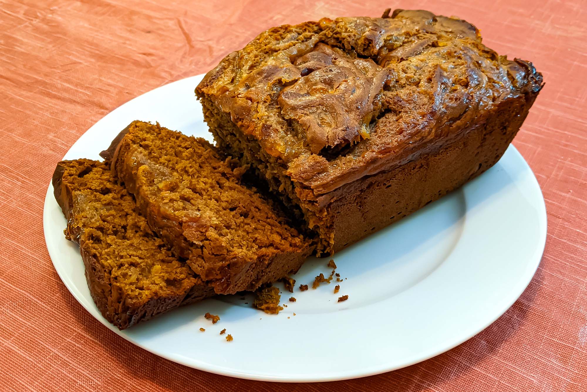 Photo: A dark loaf of dense bread has two slices cut and laid out in front of the rest of the loaf on a large white plate.