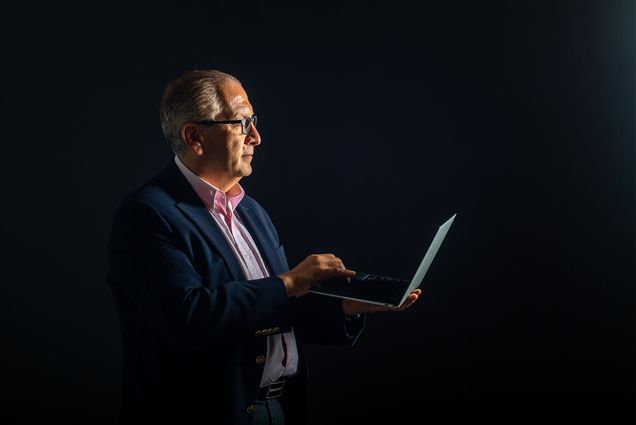 Azer Bestavros, wearing a suit against a black background, holds a laptop