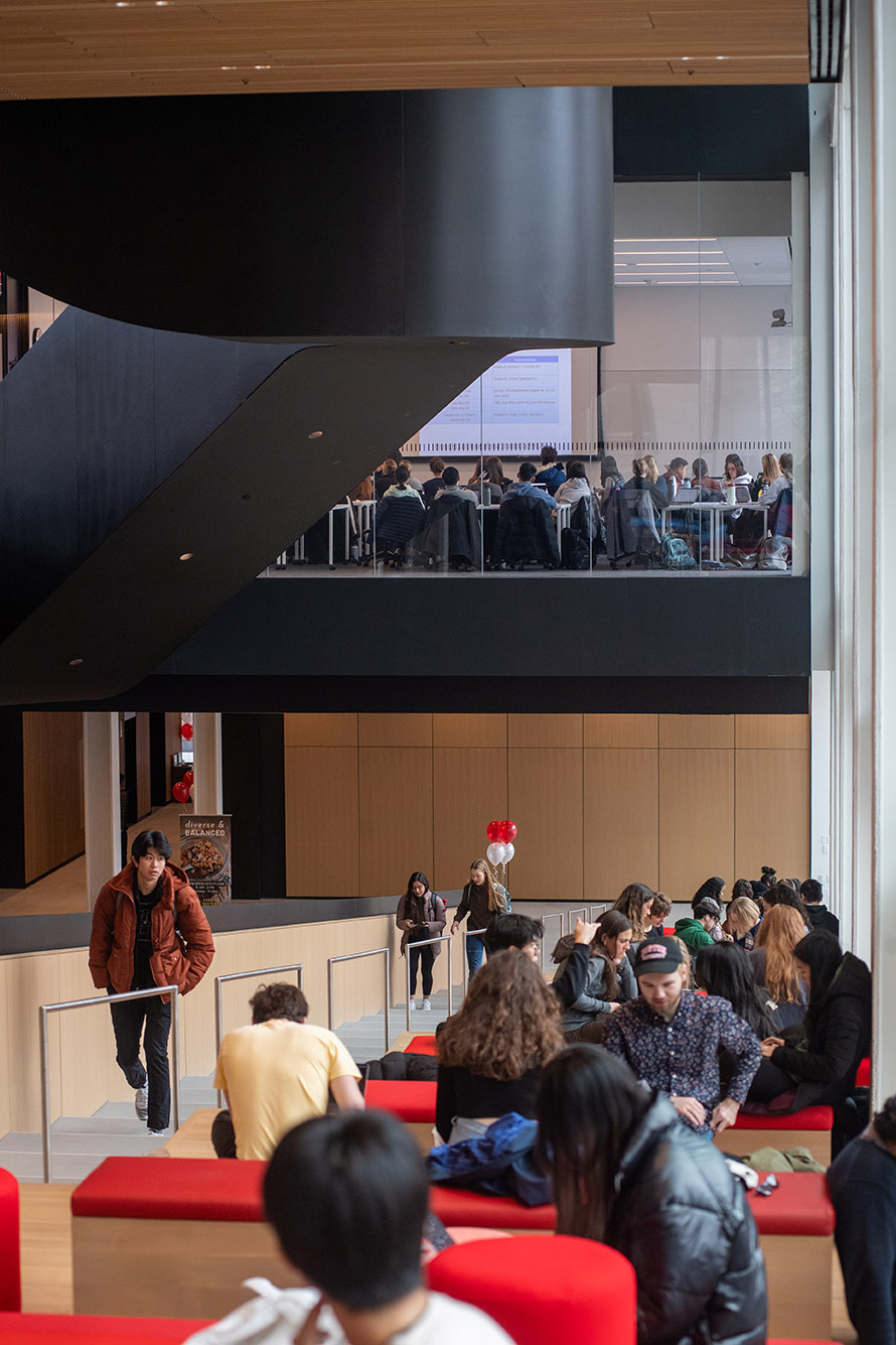 Photo: A class takes place on the second floor while students and visitors take advantage of the collaboration staircase below at the Center for Computing & Data Sciences. The upper floor shows a class taking place behind a glass wall as students sit, study, and hang out on the floor space below.
