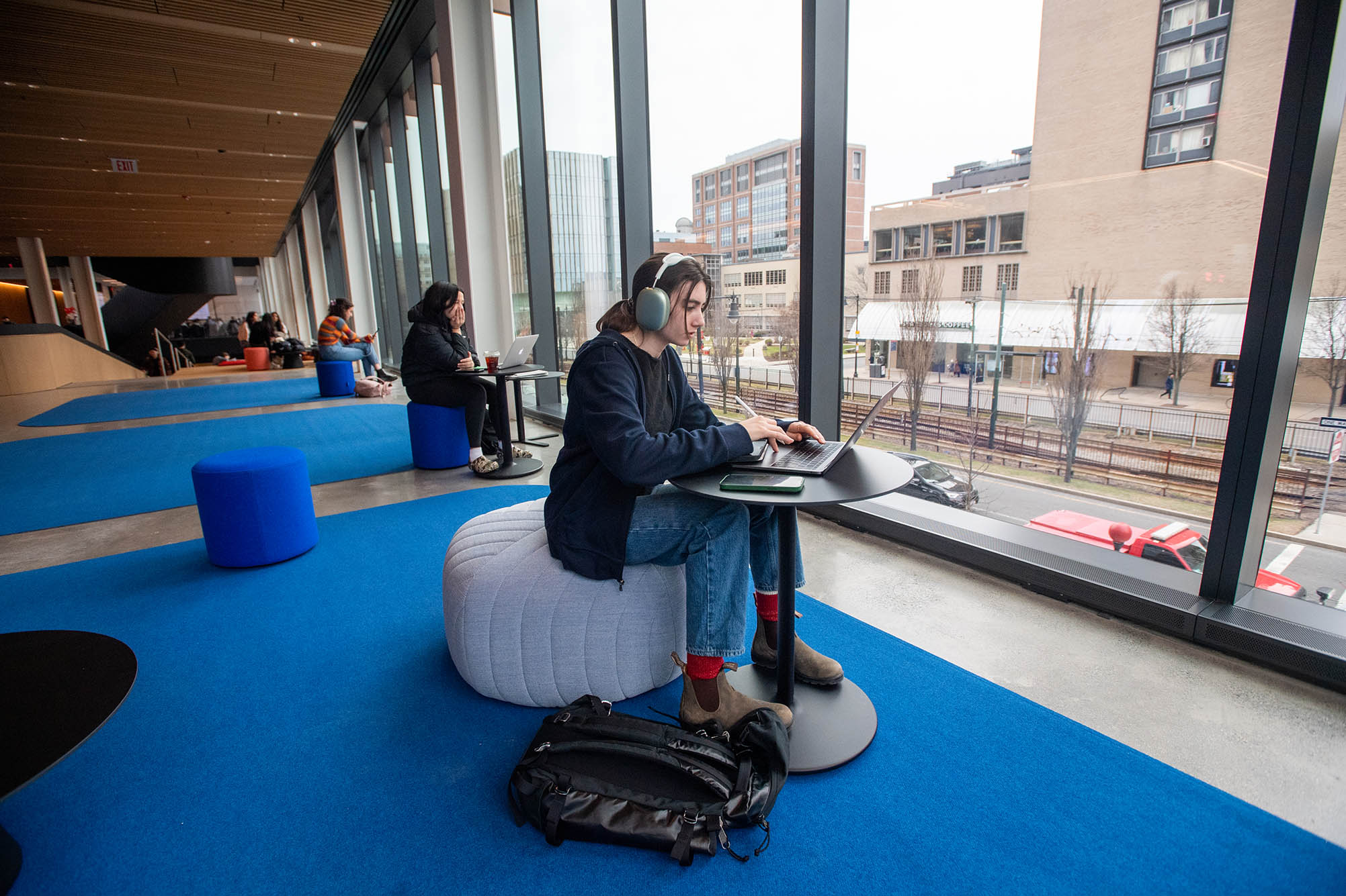 Photo: Ellen Sheker (CAS’26) looks into flights for spring break while taking advantage a well lit perch on the second floor of the Center for Computing & Data Sciences on January 19. A young woman sits in front of a large window wall as she browses on her laptop in an open sitting area.