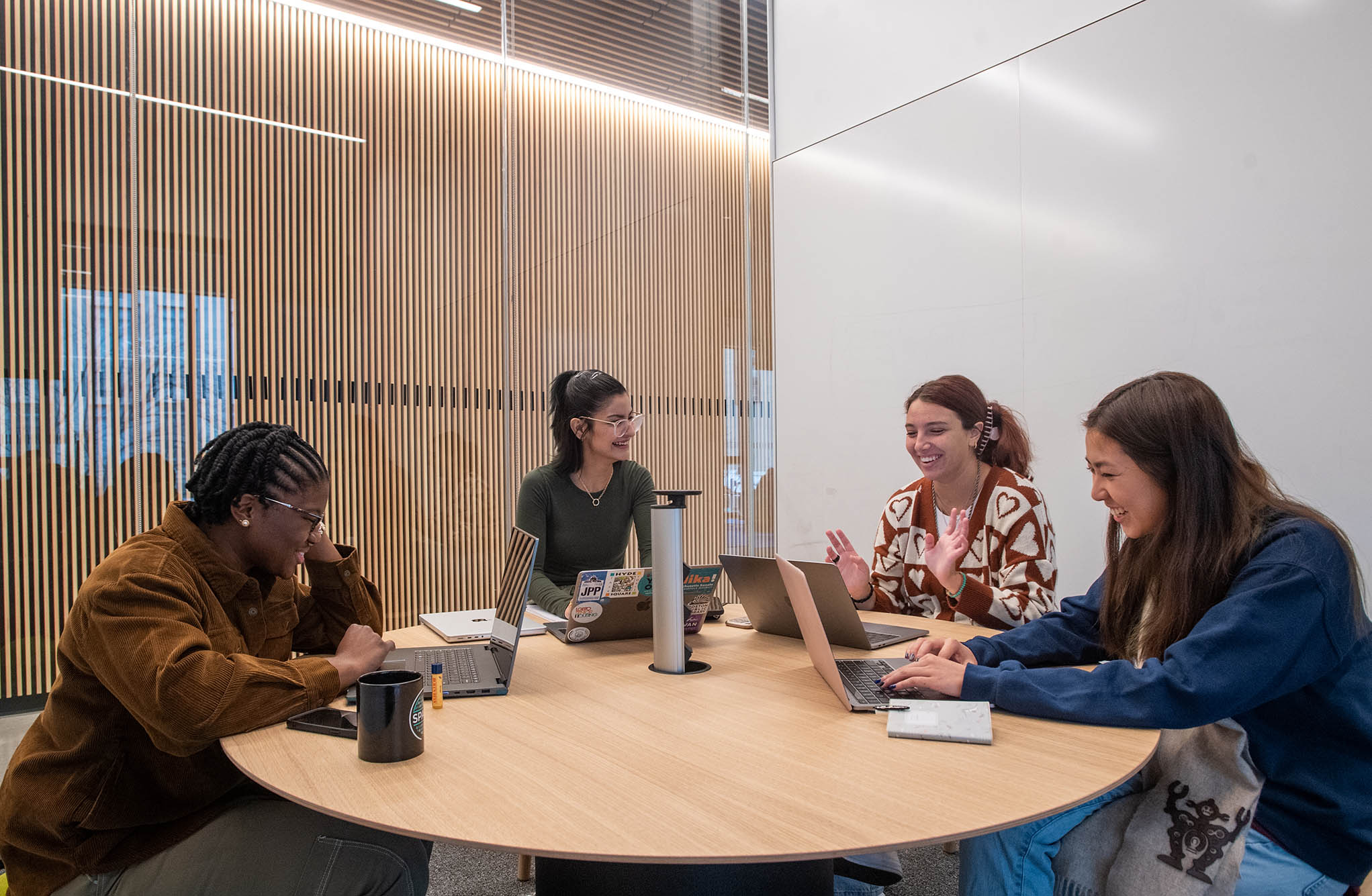 Photo: At the new SPARK location on the second floor, SPARK ambassador Anulika Nnadi (CAS’24), from left, SPARK community outreach manager Isabel Torres (CAS’19), SPARK ambassador Marina Barros (Questrom’23), and Macy So (CAS’23) meet to plan some upcoming SPARK events. Four young women sit around a round wooden table with laptops open in bright room with a wooden accent wall.