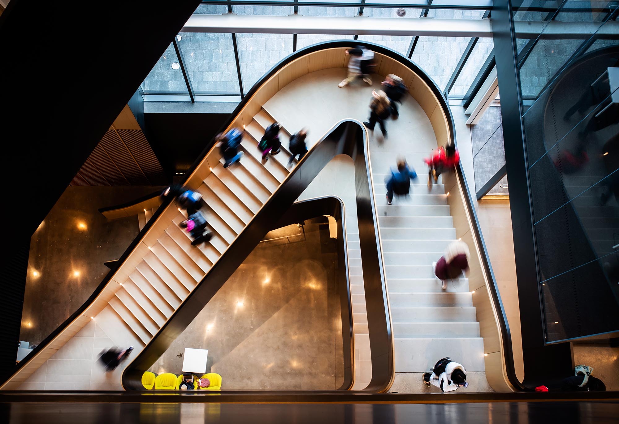 Photo: Overhead shot of students walking up and down a butterfly staircase. Students are shown as blurs as they move.