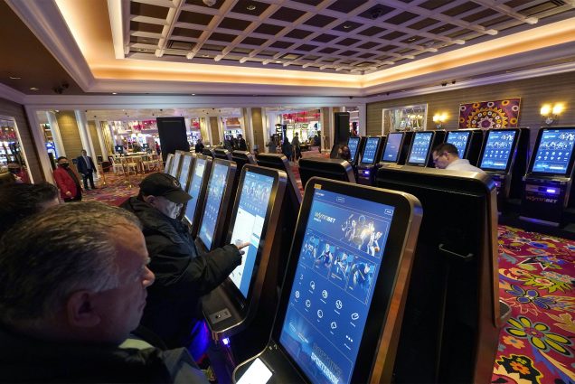 Patrons place sports bets at kiosks at Encore Boston Harbor casino, Tuesday, Jan. 31, 2023, in Everett, Mass. Massachusetts sports fans who want to wager on their favorite teams are finally getting their chance as the state kicks off sports betting at casinos in the state beginning Tuesday, Jan. 31. (AP Photo/Steven Senne)