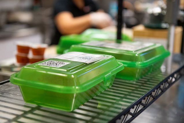 Photo: Clear green to-go containers are shown with orders in them on wire racks. They're each labeled with receipts for what is in the order.