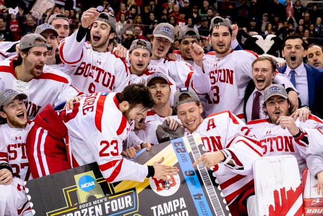 Photo: The BU 2023 Men's Hockey team celebrates and cheers on ice! They all wear the ice hockey uniforms and cheer as some point to a giant blue ticket that reads "Frozen Four".