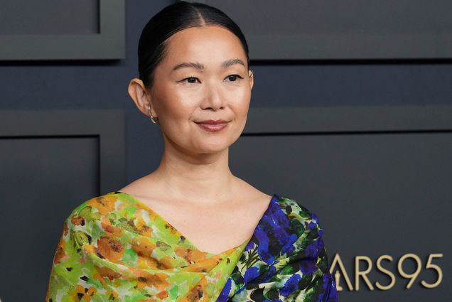 Photo: Hong Chau arrives at the 95th Annual Oscars Nominees Luncheon. An Asian woman wearing a floral, half-toned blue and green dress. She stands in front of a dark wall with a gold letter sign that reads "Oscars95"
