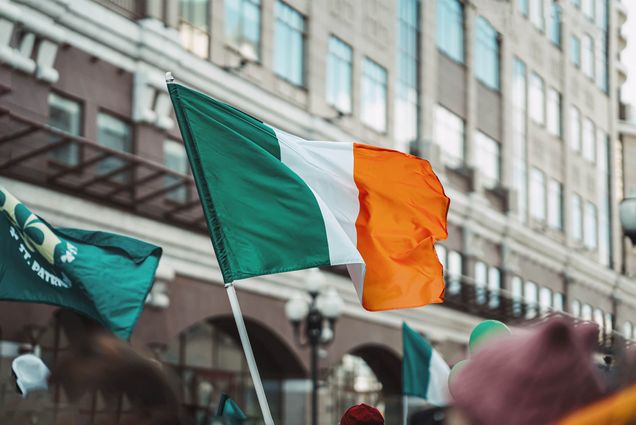 National Flag of Ireland close-up above people crowd, city street, traditional carnival of St. Patrick's Day