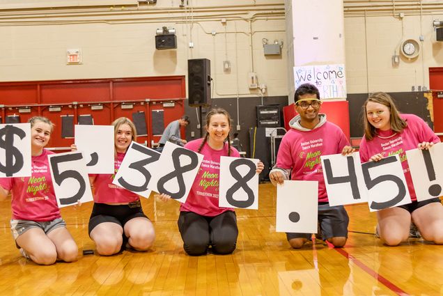 Five BU Students holding white cards with black numbers on them kneel on the floor of a gym smiling towards a camera. BU Dance Marathon raised $5,388 during TerrierTHON 2022. Photo by Matt Lutkins