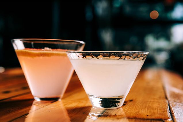 Two glasses filled with mixed alcoholic drinks on a wooden bar top