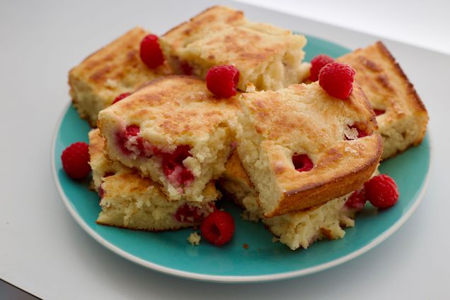 Photo: A plate of golden, fluffy pancakes decorated with red raspberries. The plate is Tiffany blue and the fluffy pancakes are cut into squares.