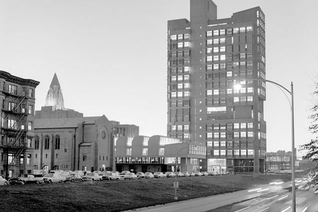 Photo: Black and white photo shows sunset traffic passing Boston University on Storrow Drive in 1964. A large lit building is shown next to a whizzing highway as old school cars are parked on the lawn nearby.