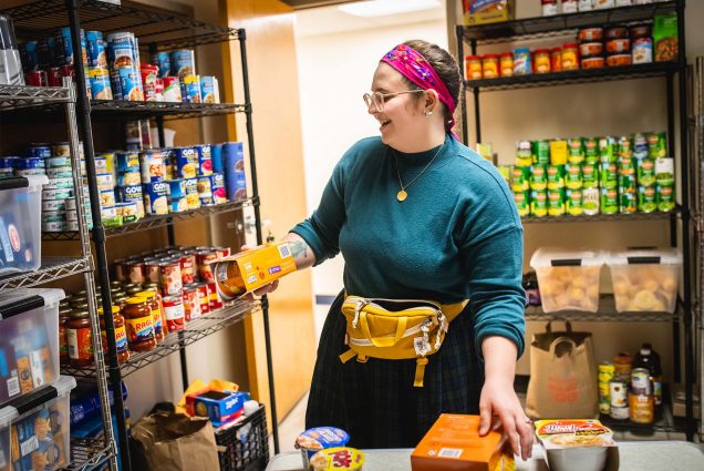 Photo: Kellie Finley-Call, a white college student with a medium build wearing a bandana and a necklace, stocks the food pantry at Wheelock College of Education and Human Development on March 27, 2023. Photo by Jackie Ricciardi for Boston University