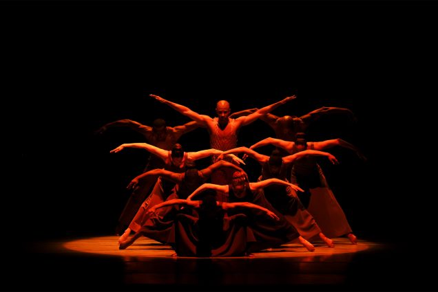 Photo: Dancers shrouded in red light make an ominous pose with their arms outstretched during a recent performance. Photo © Tony Powell. 2023 Alvin Ailey DC Gala. Kennedy Center. February 8, 2023