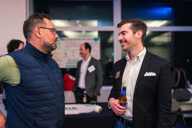 Photo: Two men who appear to be in their mid-30's talk and hold beers at a recent corporate event. The men are wearing business casual attire.