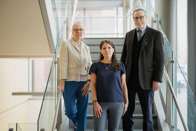 Photo: Three white individuals--Tracey Dechert, Lisa Allee, and Peter Burke--stand on a stairwell facing the camera. From left, Dechert is wearing a white blouse and cropped blazer with jeans, Allee is wearing gray slacks and a navy blouse, and Burke is in a gray blazer, black vest, and black slacks with a blue-gray button-up and tie. The area is well-lit and midday.