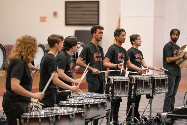 Photo: A row of BU's Drumline students in all black t-shirts perform for a showcase.