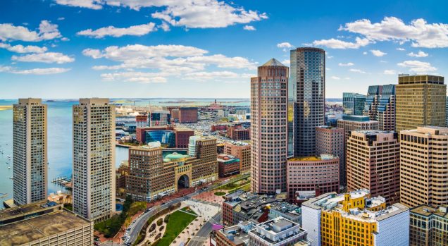 This is a stock photo of the city of Boston. You can see some of Boston's largest and most famous buildings. You can also see the bay faintly in the background. It is partly cloudy. This image is from Canva.Com